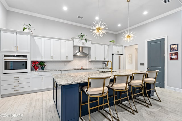 kitchen with white cabinetry, sink, wall chimney exhaust hood, white appliances, and a center island with sink