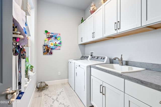 clothes washing area featuring cabinets, light hardwood / wood-style floors, washing machine and dryer, and sink