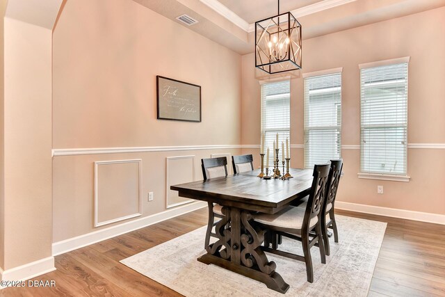 dining space with visible vents, a raised ceiling, an inviting chandelier, and wood finished floors