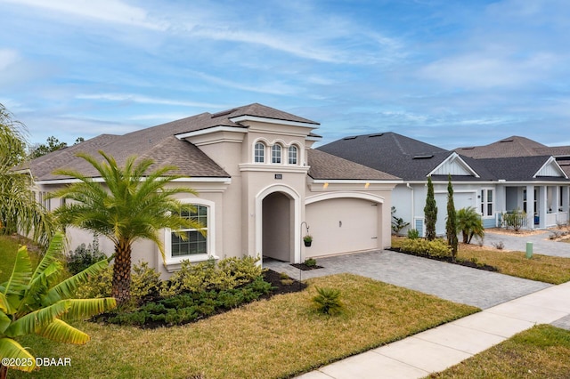 mediterranean / spanish-style house featuring a shingled roof, a front lawn, stucco siding, decorative driveway, and an attached garage