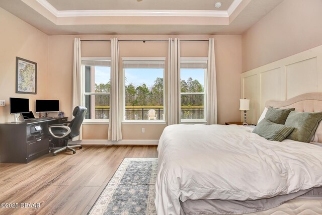 bedroom with a tray ceiling, light wood-style flooring, and crown molding