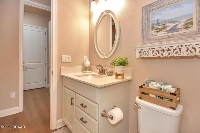 bathroom featuring baseboards, toilet, wood finished floors, and vanity