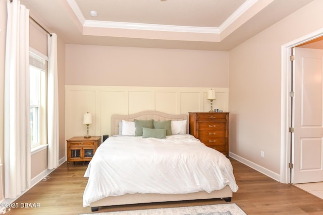 bedroom featuring a raised ceiling, a decorative wall, light wood-style floors, and ornamental molding