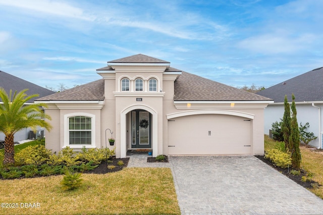 mediterranean / spanish home featuring decorative driveway, an attached garage, roof with shingles, and stucco siding