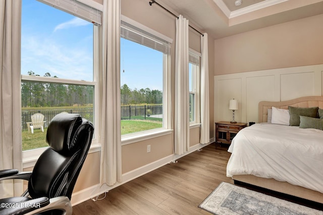 bedroom with baseboards, wood finished floors, crown molding, and a decorative wall