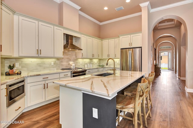 kitchen with visible vents, wall chimney range hood, appliances with stainless steel finishes, arched walkways, and a sink