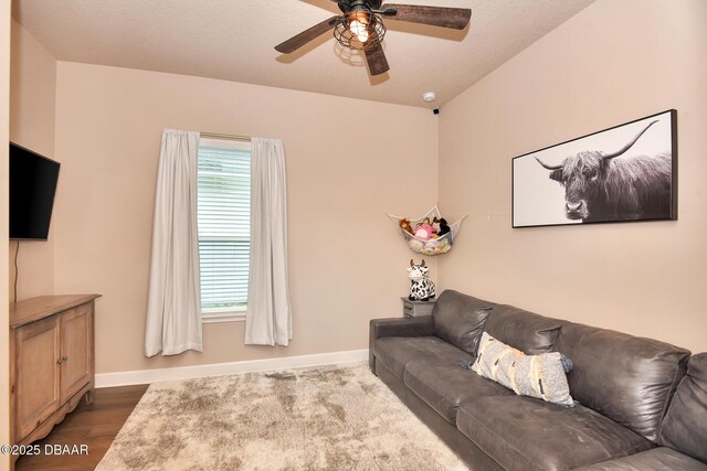 living area with baseboards, dark wood-style floors, and a ceiling fan