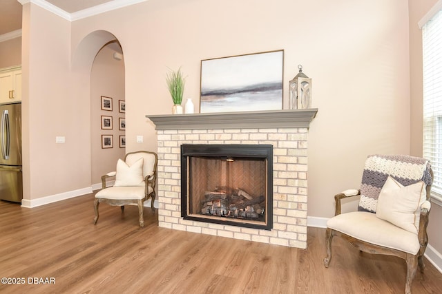 living area featuring a brick fireplace, crown molding, baseboards, and wood finished floors