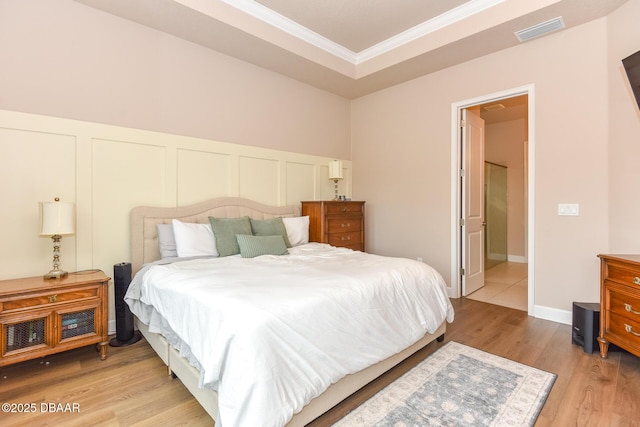 bedroom featuring light wood-type flooring, visible vents, a wainscoted wall, ornamental molding, and a decorative wall