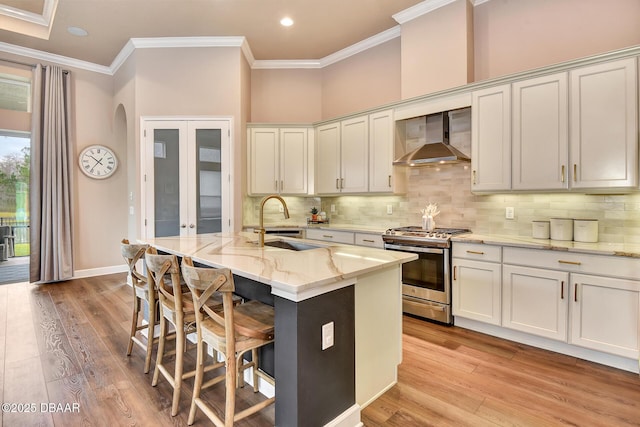 kitchen featuring gas stove, a sink, crown molding, and wall chimney range hood