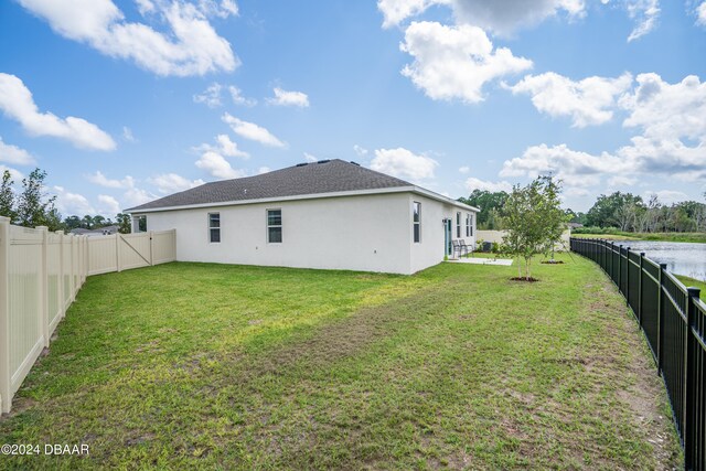 back of house with a lawn and a water view