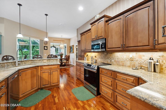 kitchen with light stone counters, hanging light fixtures, dark hardwood / wood-style flooring, and appliances with stainless steel finishes