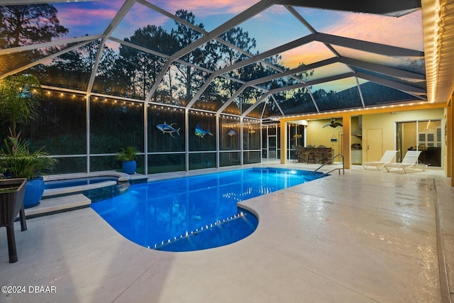 pool at dusk with a patio area, an in ground hot tub, ceiling fan, and glass enclosure