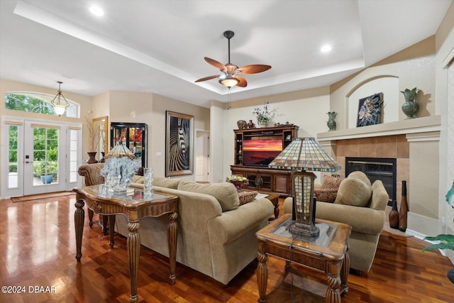 living room featuring hardwood / wood-style flooring, ceiling fan, a raised ceiling, and a tile fireplace