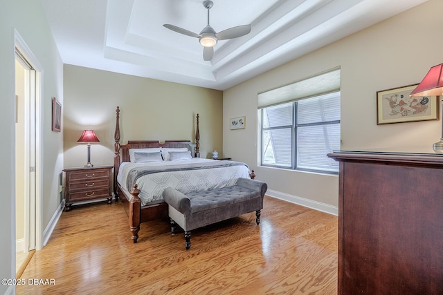 bedroom with a raised ceiling, ceiling fan, and light hardwood / wood-style floors