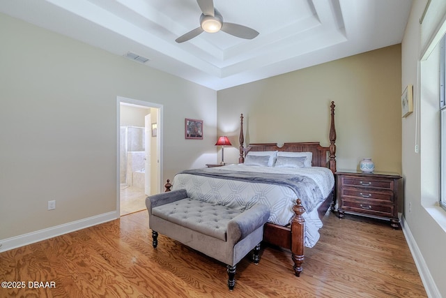 bedroom featuring ensuite bath, light wood-type flooring, ceiling fan, and a tray ceiling