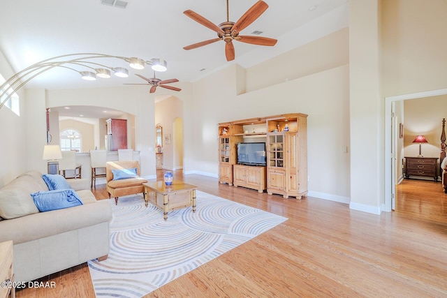 living room with a high ceiling, ceiling fan, and light hardwood / wood-style floors