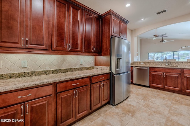 kitchen featuring stainless steel appliances, ceiling fan, light stone counters, sink, and backsplash