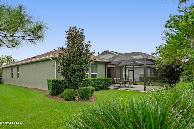 back of property with a yard, glass enclosure, and a patio area