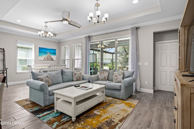 living room featuring hardwood / wood-style floors, ceiling fan with notable chandelier, a healthy amount of sunlight, and a tray ceiling