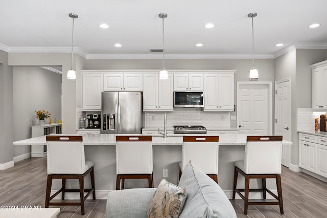 kitchen with stainless steel appliances, white cabinetry, pendant lighting, light hardwood / wood-style floors, and a kitchen island with sink