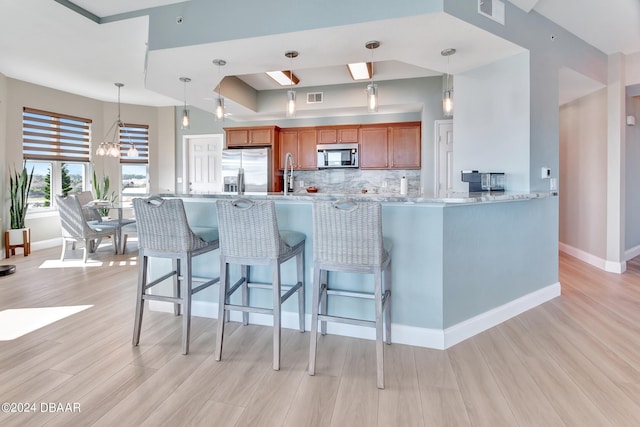 kitchen with appliances with stainless steel finishes, backsplash, hanging light fixtures, a chandelier, and light wood-type flooring