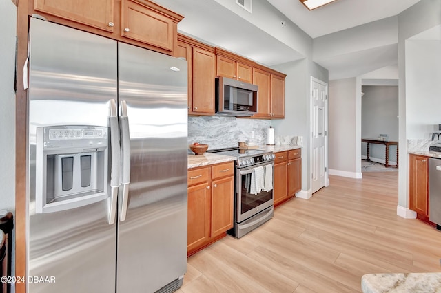 kitchen featuring stainless steel appliances, lofted ceiling, light stone counters, decorative backsplash, and light hardwood / wood-style flooring