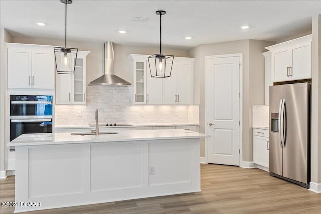 kitchen featuring a kitchen island with sink, wall chimney exhaust hood, pendant lighting, and appliances with stainless steel finishes