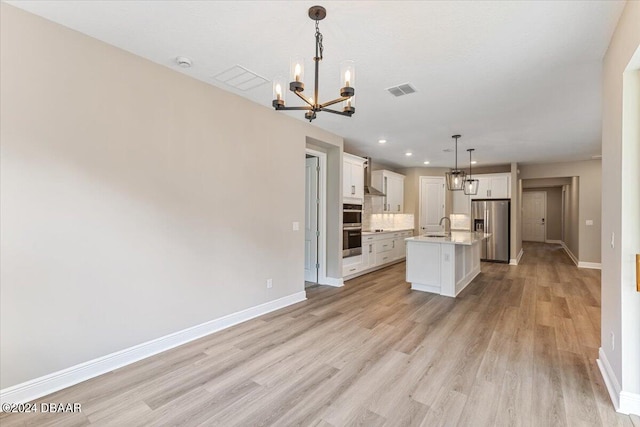 kitchen with a center island with sink, hanging light fixtures, appliances with stainless steel finishes, and light hardwood / wood-style flooring