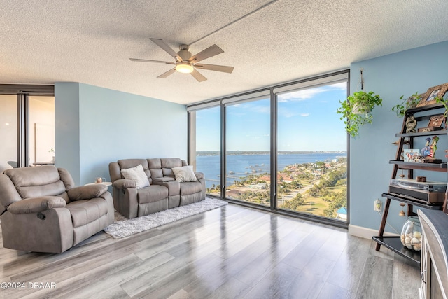 living room featuring floor to ceiling windows, a water view, light hardwood / wood-style flooring, ceiling fan, and a textured ceiling