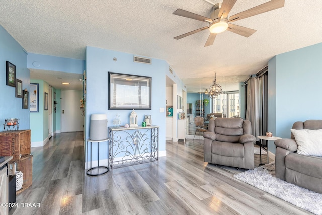 living room with ceiling fan with notable chandelier, hardwood / wood-style floors, and a textured ceiling