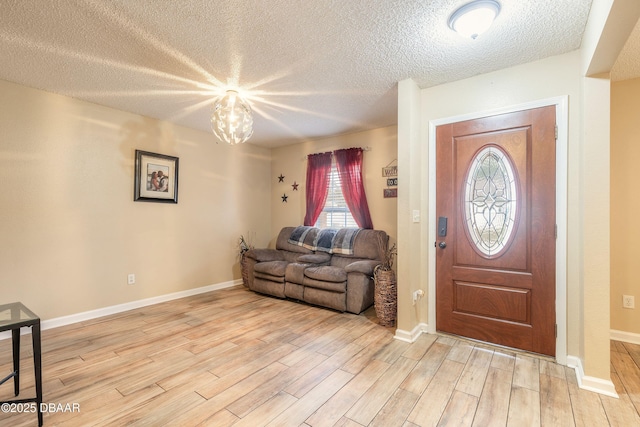 foyer entrance with light hardwood / wood-style floors, a textured ceiling, and a notable chandelier