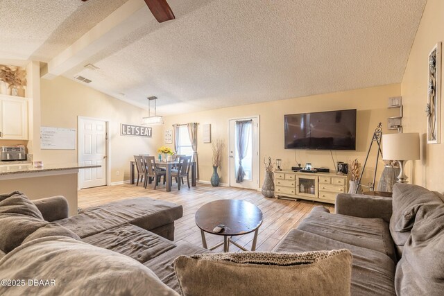 living room featuring light wood-type flooring, a textured ceiling, and lofted ceiling with beams