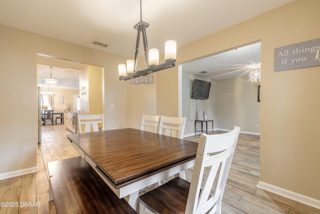 dining room with a textured ceiling, light hardwood / wood-style flooring, and a chandelier