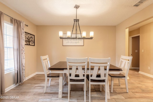 dining area with light hardwood / wood-style flooring, an inviting chandelier, and a textured ceiling