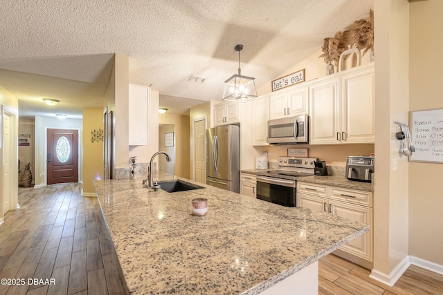 kitchen with appliances with stainless steel finishes, decorative light fixtures, sink, kitchen peninsula, and light stone counters