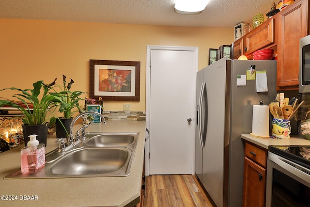 kitchen with stainless steel appliances, a textured ceiling, sink, and light hardwood / wood-style flooring