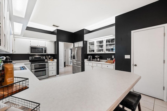 kitchen featuring a kitchen breakfast bar, white cabinetry, stainless steel appliances, and light tile patterned floors