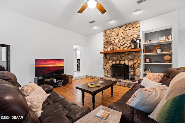 living room featuring built in shelves, ceiling fan, a stone fireplace, and hardwood / wood-style floors