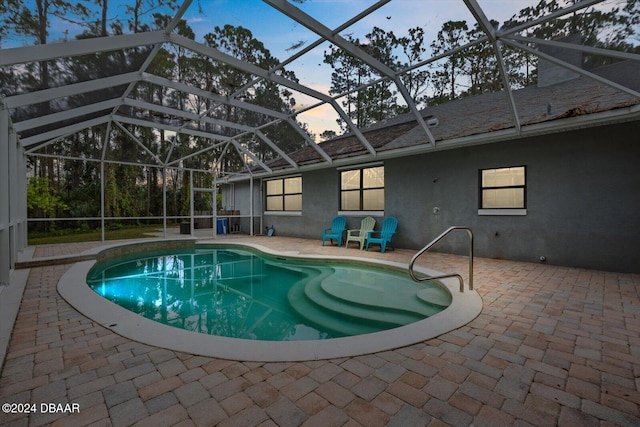 pool at dusk featuring glass enclosure and a patio area