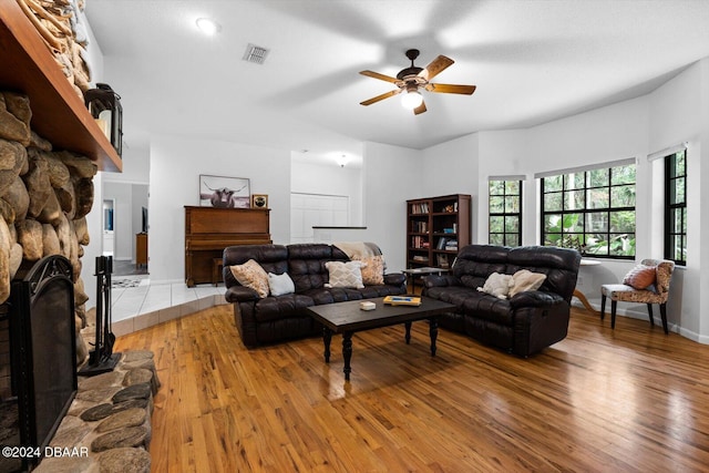 living room featuring ceiling fan, a stone fireplace, and wood-type flooring