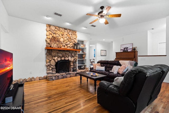 living room with built in shelves, a stone fireplace, ceiling fan, and hardwood / wood-style floors