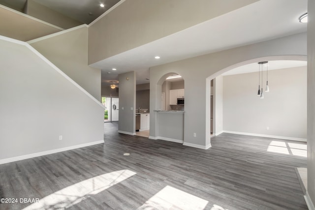 unfurnished living room featuring dark wood-type flooring, ceiling fan, and a high ceiling