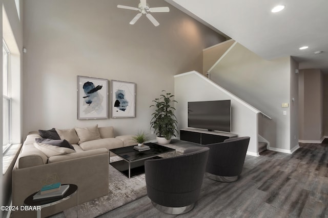 living room with dark wood-type flooring, a towering ceiling, ceiling fan, and a healthy amount of sunlight