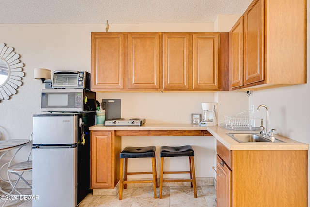 kitchen with a breakfast bar area, a textured ceiling, sink, and appliances with stainless steel finishes