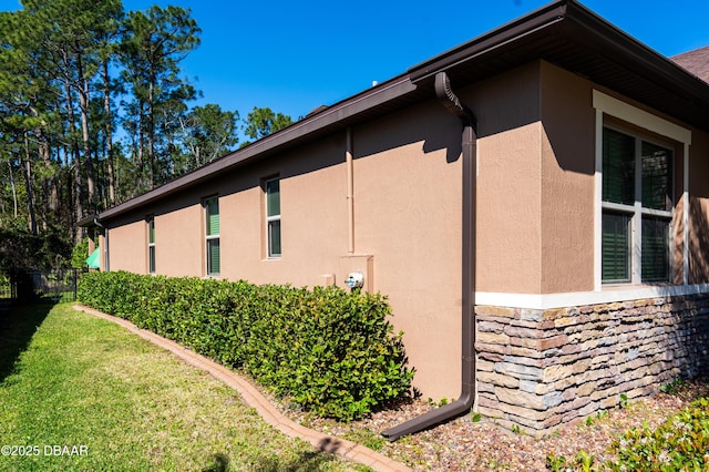 view of property exterior with stone siding, stucco siding, a lawn, and fence