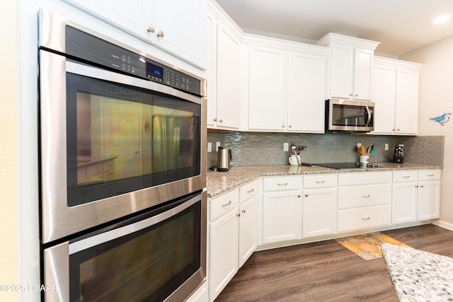 kitchen with light stone counters, decorative backsplash, white cabinets, stainless steel appliances, and dark wood-style flooring