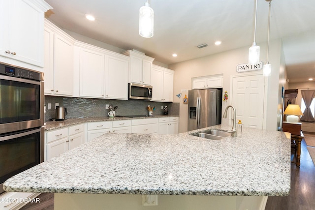 kitchen featuring visible vents, a sink, backsplash, stainless steel appliances, and a large island with sink