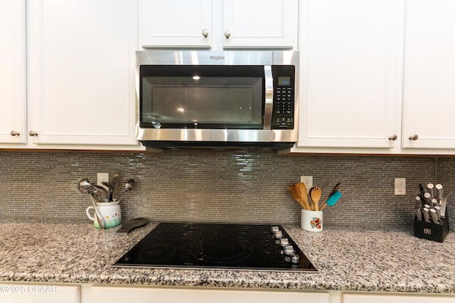 details with black electric cooktop, light stone counters, stainless steel microwave, white cabinetry, and decorative backsplash