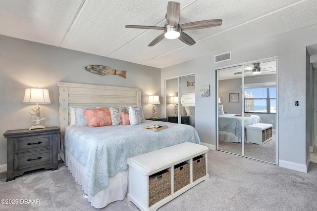 carpeted bedroom with ceiling fan, a textured ceiling, and two closets